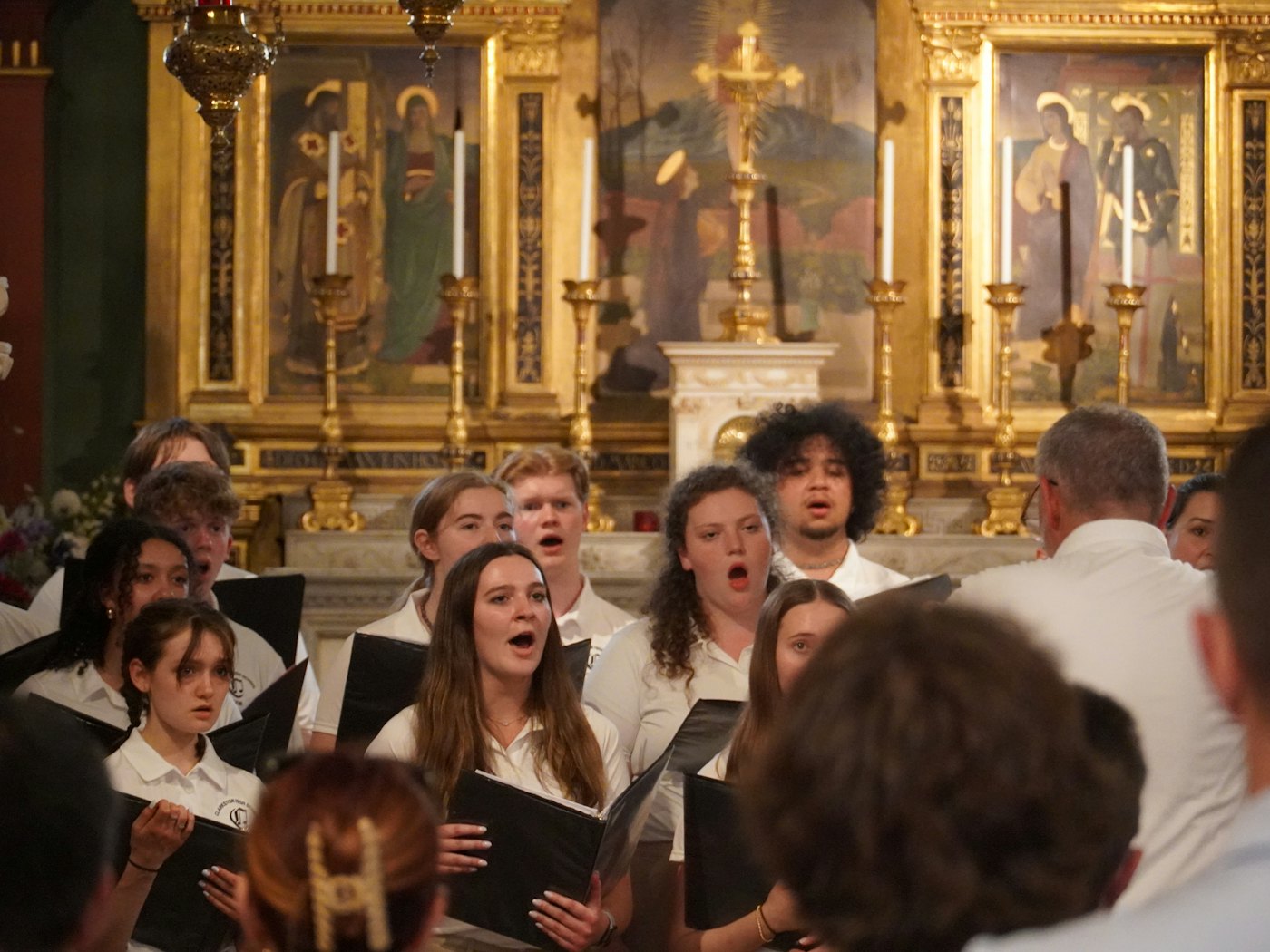 A young choir singing from their folders in a gilded chapel