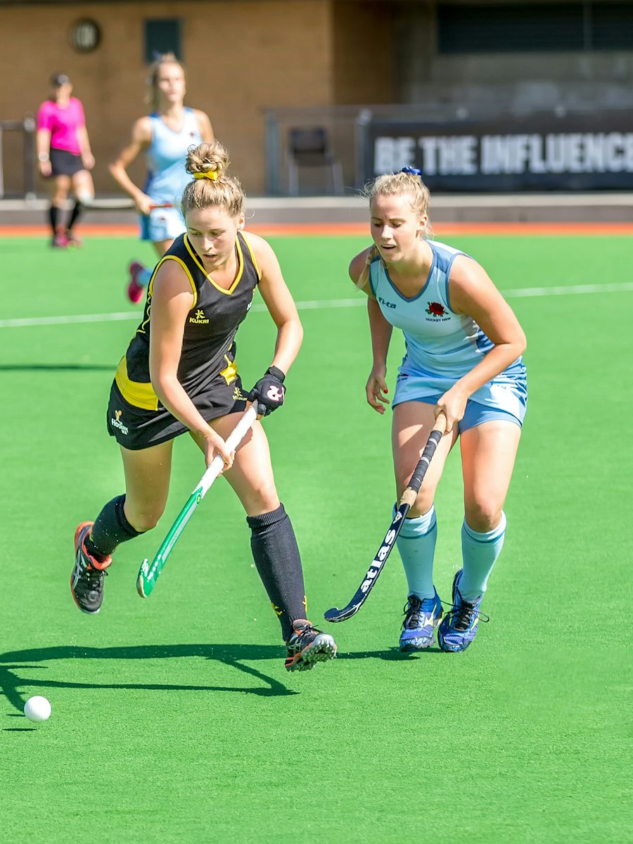 Two hockey players chasing the ball across a bright green pitch