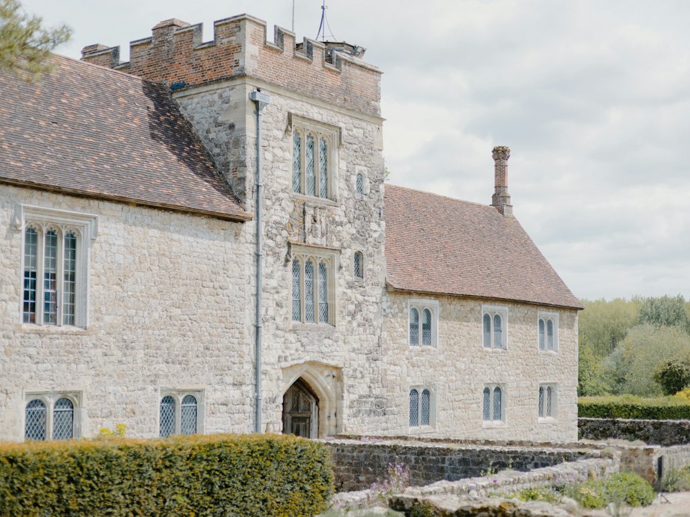 A stone manor house with a battlemented tower behind a clipped hedge