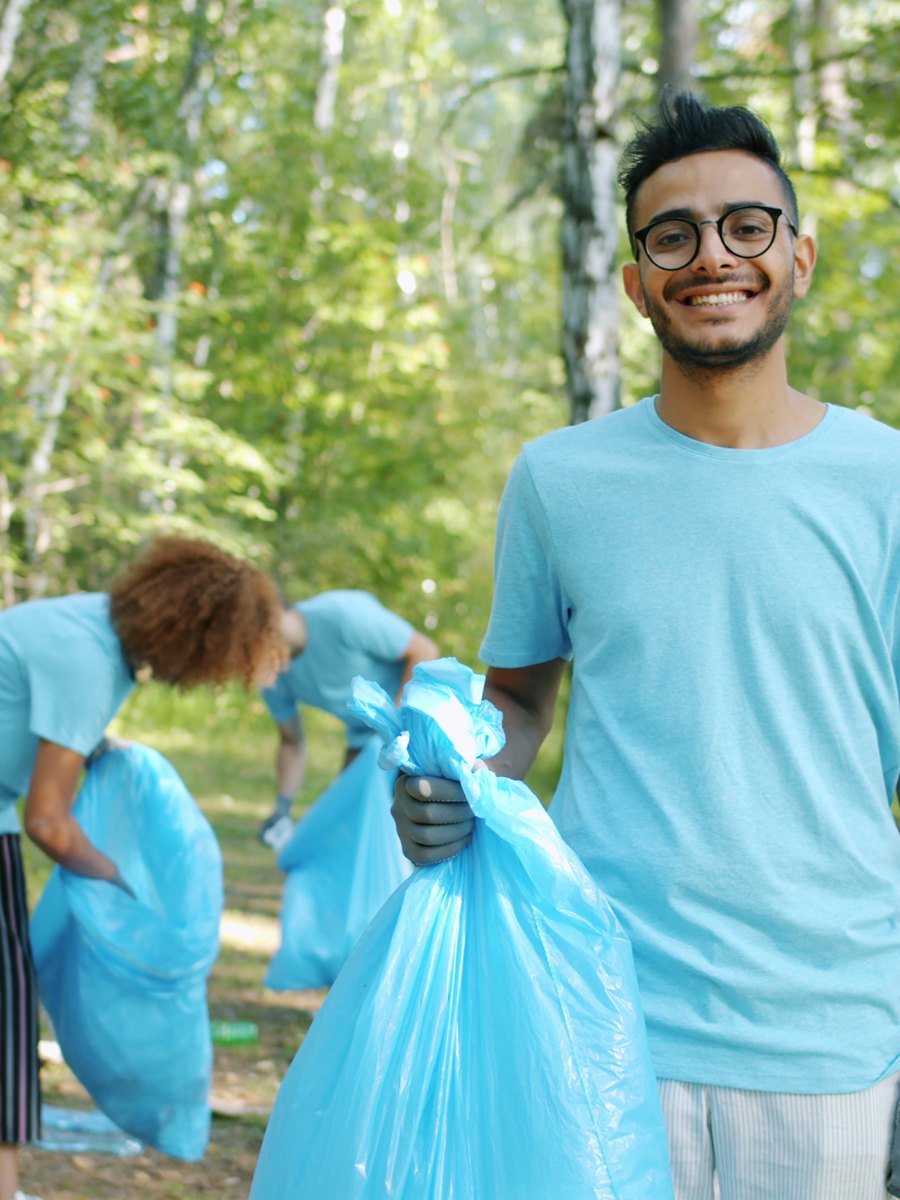 A smiling young volunteer holding a filled bag during a woodland litter pick