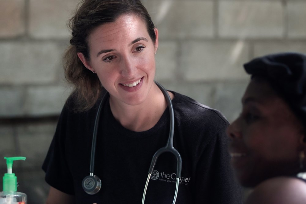 A nurse with a stethoscope smiling as she talks with a patient