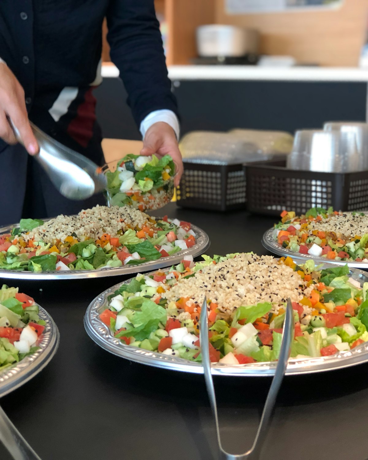 Fresh salads being served with tongs from large platters at a lunch counter