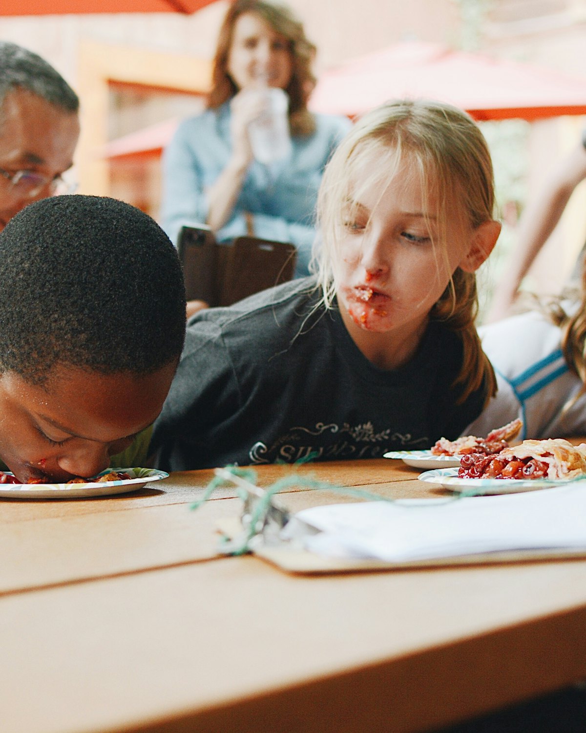 Children leaning over their plates and laughing during a meal at a shared table